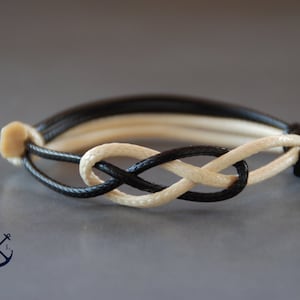 May include: Black and white braided bracelet with a knot in the shape of an infinity symbol.