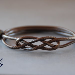 May include: A brown braided cord bracelet with a knot design. The bracelet is made of a thick, durable cord and is tied with a secure knot.