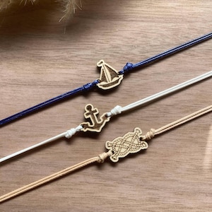 Peut inclure: Trois bracelets avec des breloques en bois sur le thème nautique. Le premier bracelet est bleu avec un charme de voilier. Le deuxième bracelet est blanc avec un charme d'ancre. Le troisième bracelet est beige avec un charme de nœud de corde.