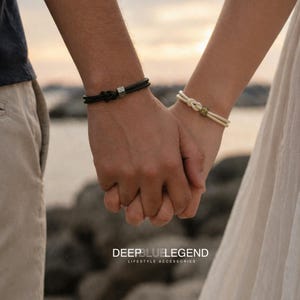 May include: Two matching bracelets are displayed, one black and one cream. The black bracelet features a silver accent, and the cream bracelet has a gold accent. The bracelets are worn on wrists, with hands clasped. The brand name "DEEPBLUELEGEND" is visible.