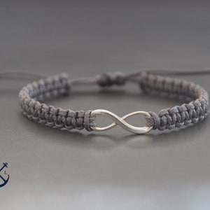 Puede incluir: Una pulsera trenzada gris con un dije de plata en forma de infinito.