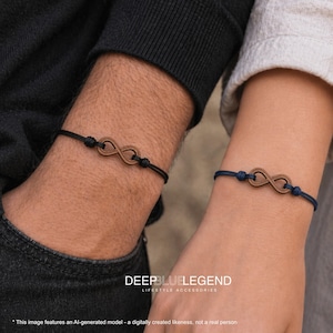 Op de afbeelding: Twee armbanden met een bruin houten oneindigheidssymbool in het midden van een dun koord. De ene armband heeft een zwart koord en de andere een donkerblauw koord. Beide koorden zijn vastgezet met verstelbare knopen naast het houten symbool.