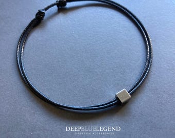May include: Black cord bracelet with a small, silver-colored square bead. The bracelet is adjustable with a sliding knot closure. The text "DEEPBLUELEGEND LIFESTYLE ACCESSORIES" is at the bottom of the image.