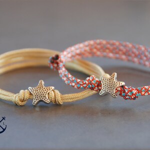 May include: Two friendship bracelets with a starfish charm. One bracelet is beige and the other is red, white, and blue.