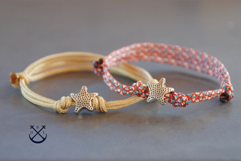 May include: Two friendship bracelets with a starfish charm. One bracelet is beige and the other is red, white, and blue.