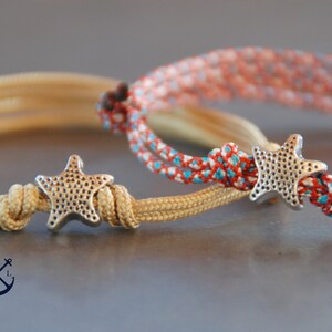 May include: Two friendship bracelets with silver starfish charms. One bracelet is beige and the other is red, white, and blue.