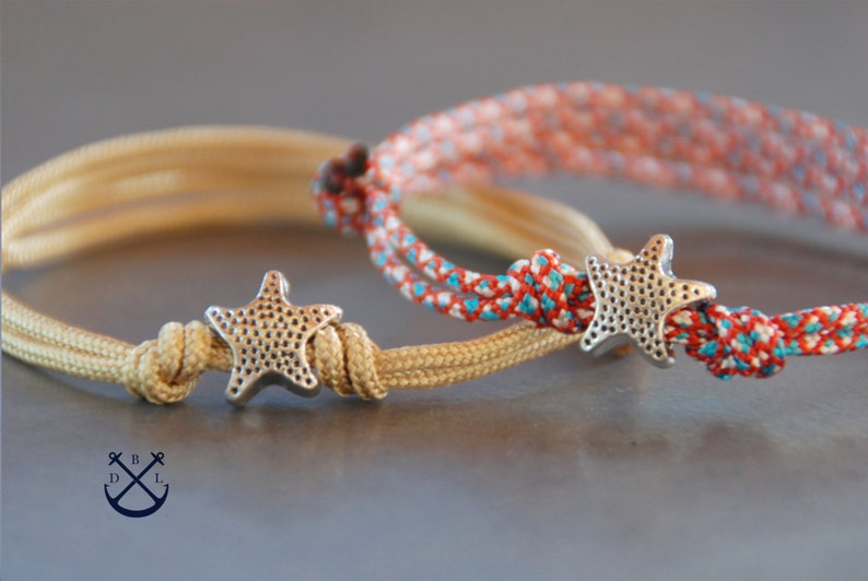 May include: Two friendship bracelets with silver starfish charms. One bracelet is beige and the other is red, white, and blue.
