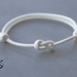 May include: A white rope bracelet with a knot in the center. The bracelet is made of a thick, braided rope.
