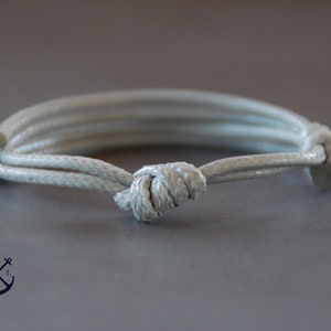 Könnte beinhalten: Ein weißes Seil-Armband mit einem geknoteten Design. Das Armband besteht aus drei Seilsträngen.