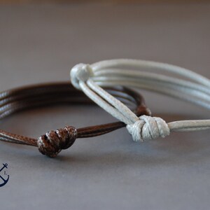 May include: Two braided leather bracelets, one brown and one white, with knotted closures.