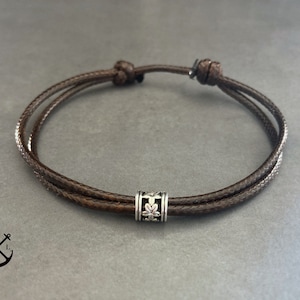 Peut inclure: Un bracelet en cordon de cuir marron avec un fermoir en argent orné d'un motif floral.