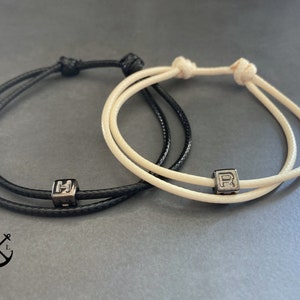 Op de afbeelding: Twee vriendschapsarmbanden, een zwarte en een witte, met zilveren bedelarmbanden. De kralen hebben de letters "H" en "R" erop.