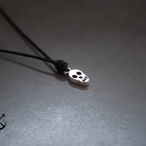 Puede incluir: Un collar con un colgante de calavera de plata en un cordón negro.