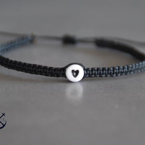 Peut inclure: Un bracelet tressé noir avec un charme en forme de cœur blanc.