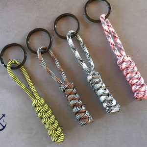 Könnte beinhalten: Vier bunte Paracord-Schlüsselanhänger mit verschiedenen Mustern. Jeder Schlüsselanhänger hat einen schwarzen Metallring.