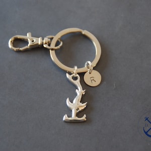 Könnte beinhalten: Silberner Schlüsselanhänger mit einem Hai-Flossen-Anhänger, einem runden Anhänger mit dem eingravierten Buchstaben "R" und einem silbernen geteilten Ring.