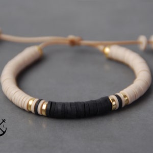 Op de afbeelding: Een beige en zwarte kralen armband met een gouden accent. De armband is gemaakt met ronde kralen en heeft een eenvoudig, minimalistisch ontwerp.