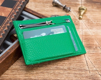 Puede incluir: Una cartera de cuero verde con cierre de cremallera y una ranura para tarjeta que dice "AMERICAN EXPRESS".