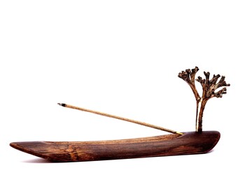 May include: A wooden incense holder with a dried branch design. A single incense stick is burning in the holder.