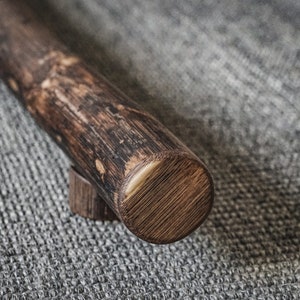 May include: A close-up of a dark brown wooden handrail with a rounded end. The handrail is mounted on a gray textured surface.