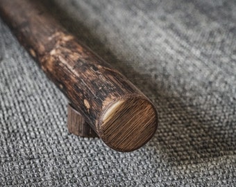 May include: A close-up of a dark brown wooden handrail with a rounded end. The handrail is mounted on a gray textured surface.
