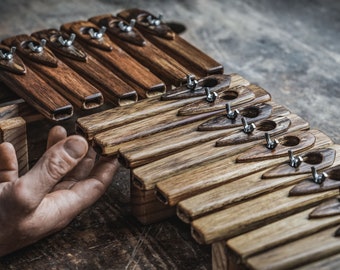 May include: A set of wooden musical instruments, known as a kalimba, with a hand resting on the top. The kalimba is made of dark wood with metal tuning keys.