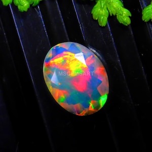 Può includere: Pietra preziosa di opale di forma ovale con una base bianca e colori arcobaleno iridescenti, tra cui rosso, arancione, giallo, verde, blu e viola. La pietra preziosa è sfaccettata e ha un'alta lucidatura.
