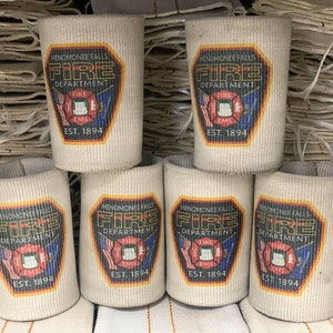 May include: Six white fabric can coolers with a black and red fire department logo. The logo says "Menomonee Falls Fire Department" with a fire hydrant and the words "Fire EMS" and "Est. 1894".