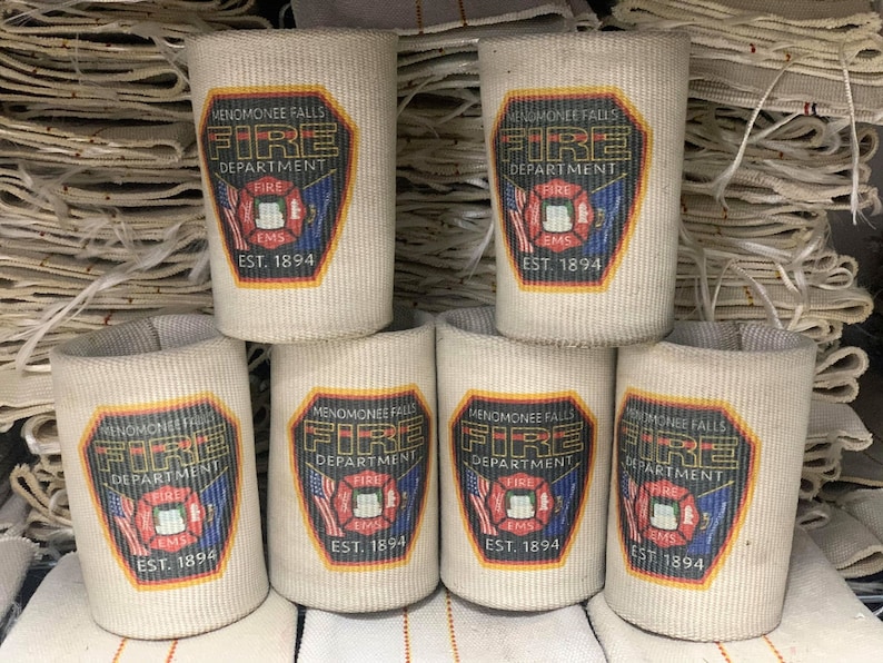 May include: Six white fabric can coolers with a black and red fire department logo. The logo says "Menomonee Falls Fire Department" with a fire hydrant and the words "Fire EMS" and "Est. 1894".