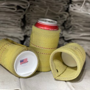 Puede incluir: Tres enfriadores de latas amarillos hechos de material tejido. Uno contiene una lata roja y blanca, otro tiene una tapa blanca con una peque&ntilde;a pegatina de la bandera estadounidense. Los enfriadores tienen costuras rojas y un lazo.
