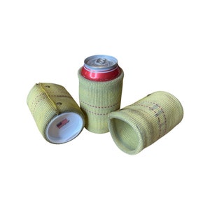 May include: Three yellow can coolers with red stitching. One cooler holds a red and silver can. The coolers are made of a woven material and have a white bottom with a small American flag sticker.