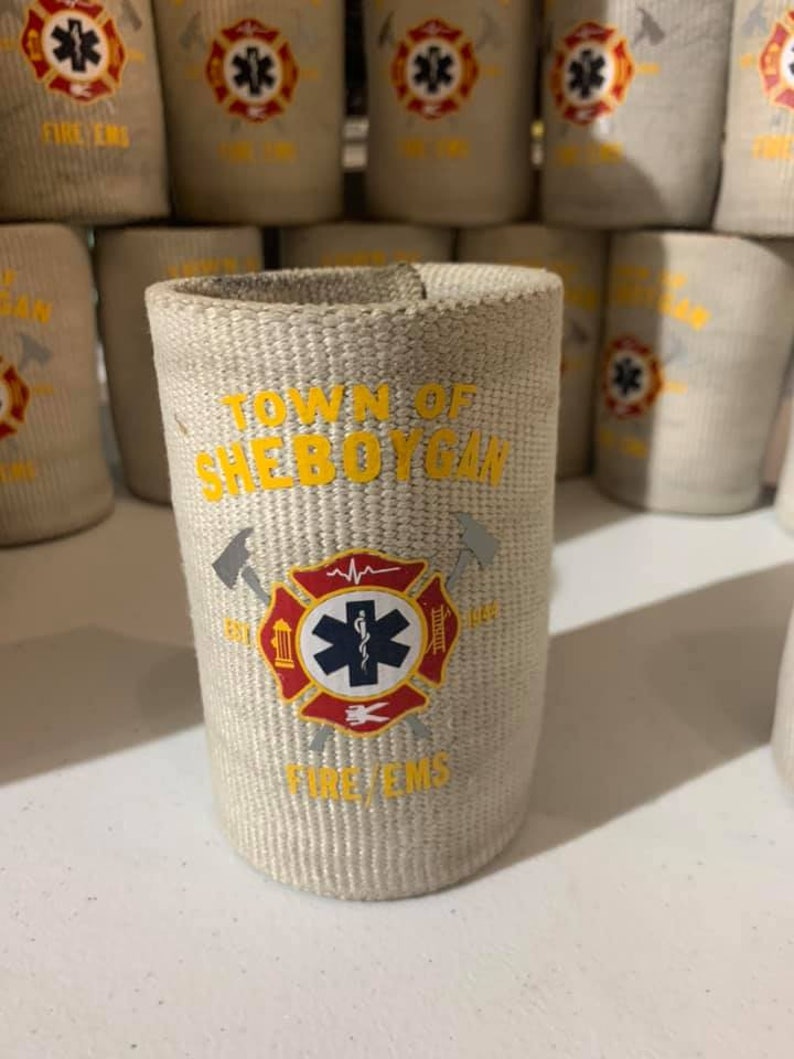 May include: A white fabric can cooler with the text "Town of Sheboygan" in yellow. The cooler has a red and yellow fire department logo with a star of life and the words "Fire/EMS".