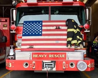 May include: A red fire truck with the words "Heavy Rescue" on the front. An American flag is displayed on the front of the truck, and a firefighter's jacket is hanging on the side.