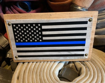 May include: A framed American flag with a thin blue line across the center, mounted on a wooden frame with a distressed finish.