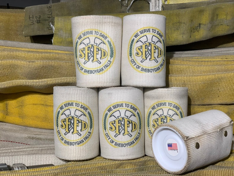 May include: Six white canvas can coolers with a yellow and green logo that reads "We Serve To Save SFFD City of Sheboygan Falls".