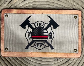 May include: A wooden framed sign with a white canvas background featuring a black and red firefighter emblem with the words "FIRE DEPT." and a thin red line.