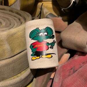 May include: A white canvas fire hose wrap with a cartoon mouse wearing a red shirt with the text "RShee" and holding a wrench. The mouse is green, yellow, and black.