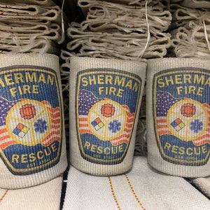 May include: Three beige fire hose wraps with the text "Sherman Fire Rescue Est. 1872" printed on each. The logo features a red, yellow, and blue fire department symbol with an American flag design.