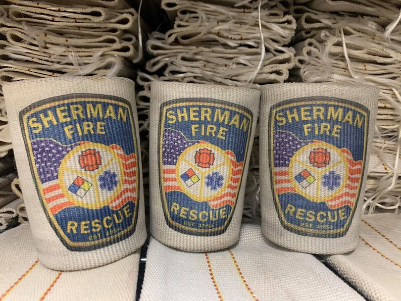 May include: Three beige fire hose wraps with the text "Sherman Fire Rescue Est. 1872" printed on each. The logo features a red, yellow, and blue fire department symbol with an American flag design.