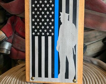 May include: A wooden framed canvas print with a thin blue line running down the center. The canvas features a silhouette of a police officer standing in front of an American flag.