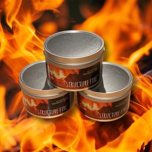 Peut inclure: Trois boîtes de bougies en métal argenté avec un motif de flammes rouge, orange et jaune et le texte "Structure Fire" sur chacune. Les bougies sont placées sur un fond de flammes orange et jaunes.
