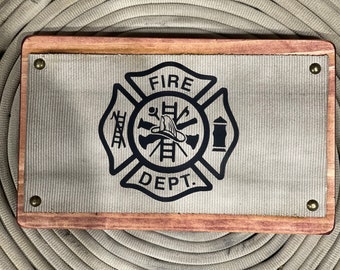 May include: A wooden plaque with a beige canvas insert featuring a black firefighter emblem with the words "FIRE DEPT."