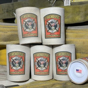 May include: Six white canvas can coolers with a red, yellow, and black logo that says "Firehouse Cookie Company" and a cartoon image of a firefighter. The logo is surrounded by a red border. The can coolers are stacked on top of each other. The background is a yellow fire hose.
