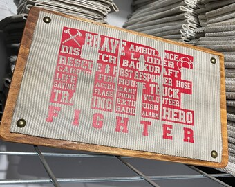 May include: A wooden sign with a white canvas background and red text. The sign reads "BRAVE FIRE FIGHTER" and includes words related to firefighting, such as "rescue", "ambulance", "ladder", and "first responder".