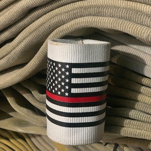 May include: A white fabric sleeve with a red, white, and blue American flag design and a thin red stripe across the middle. The sleeve is sitting on top of a stack of beige fire hoses.