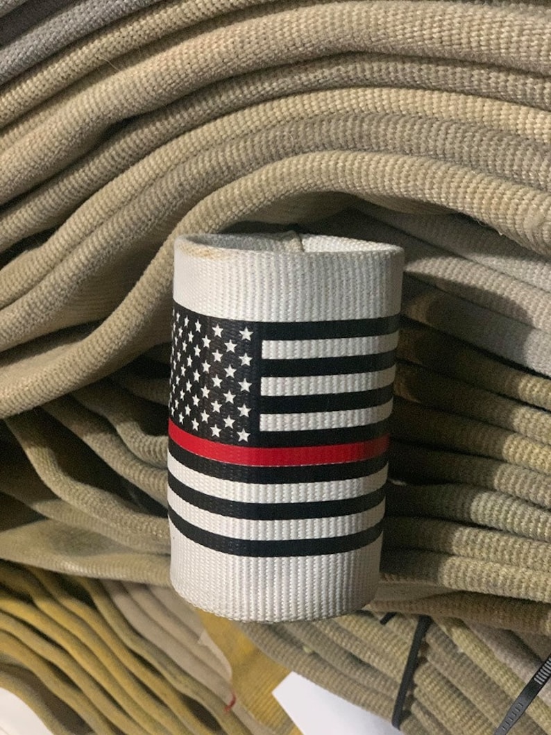 May include: A white fabric sleeve with a red, white, and blue American flag design and a thin red stripe across the middle. The sleeve is sitting on top of a stack of beige fire hoses.