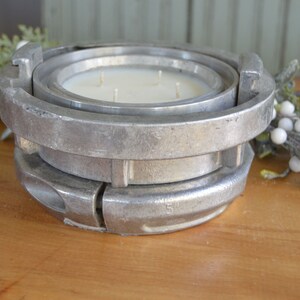 May include: A white candle with three wicks sits in a silver metal candle holder. The holder is made of two pieces that fit together.