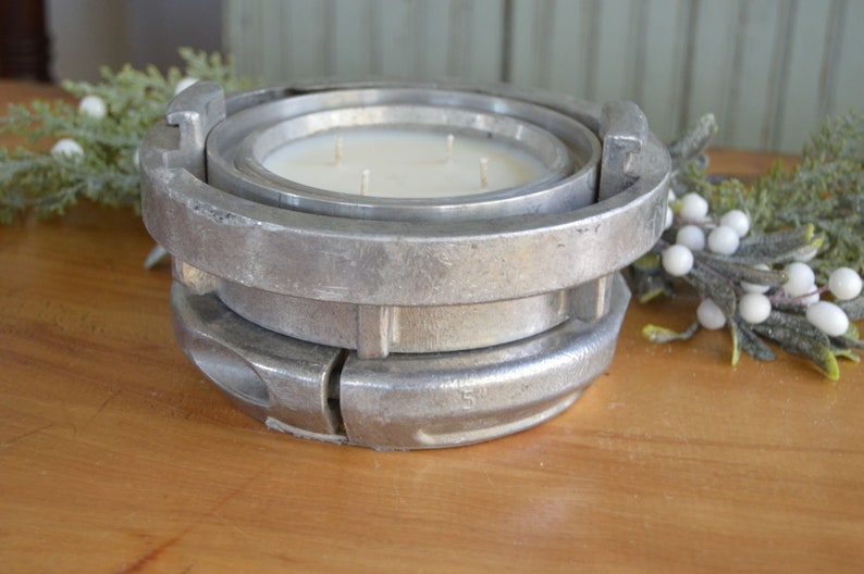 May include: A white candle with three wicks sits in a silver metal candle holder. The holder is made of two pieces that fit together.