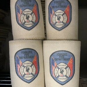 May include: Four white canvas fire hose wraps with blue and red printed logos. Each logo features the words "Yonkers Fire Department" and a crest with the words "Integrity, Valor, Loyalty, Dedication".