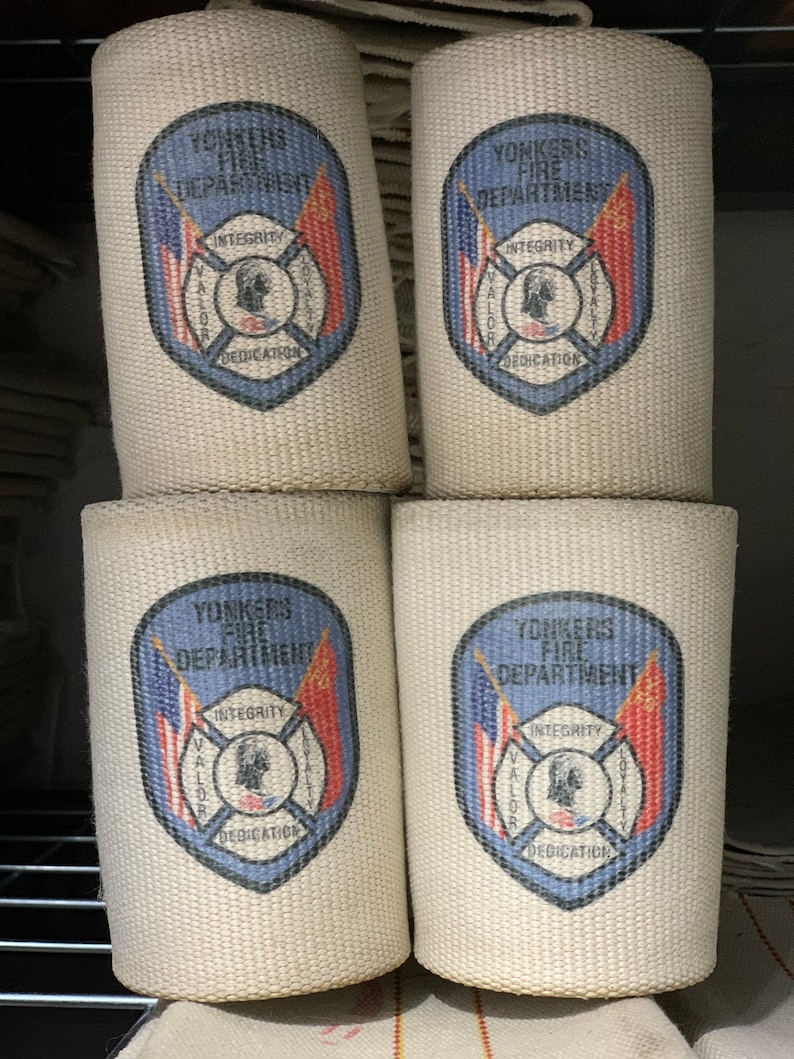 May include: Four white canvas fire hose wraps with blue and red printed logos. Each logo features the words "Yonkers Fire Department" and a crest with the words "Integrity, Valor, Loyalty, Dedication".